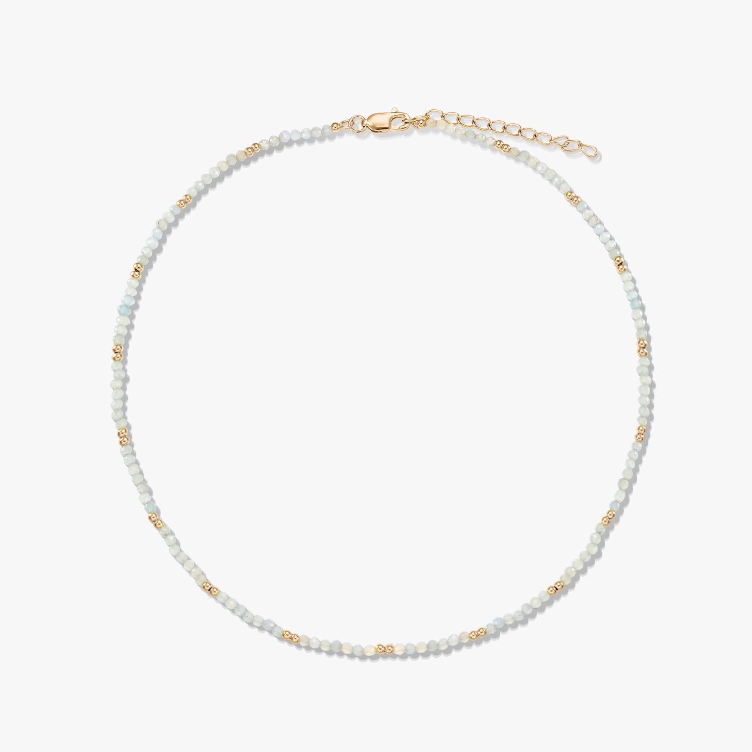 Collana delicata a perline di pietra di luna con piccole perline distanziatrici dorate e chiusura a moschettone con prolunga in argento sterling placcato oro, disposta in cerchio su sfondo bianco.