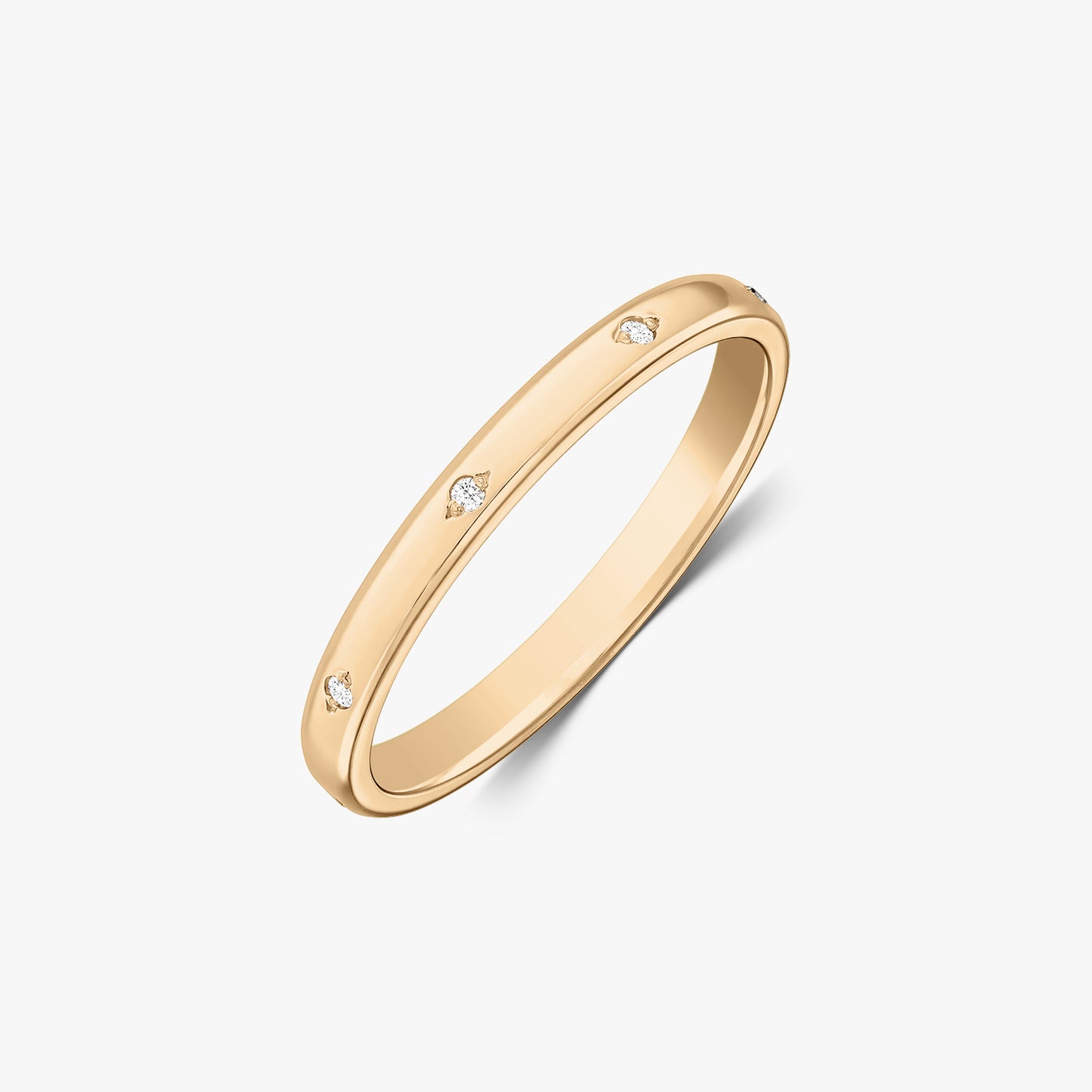 Scatto in studio angolato di una fede nuziale sottile in oro giallo 14K con piccoli diamanti incastonati a filo, su sfondo bianco.