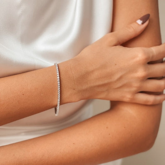 Primo piano del braccio di una donna con un bracciale tennis in argento e zirconi, su sfondo di raso bianco.
