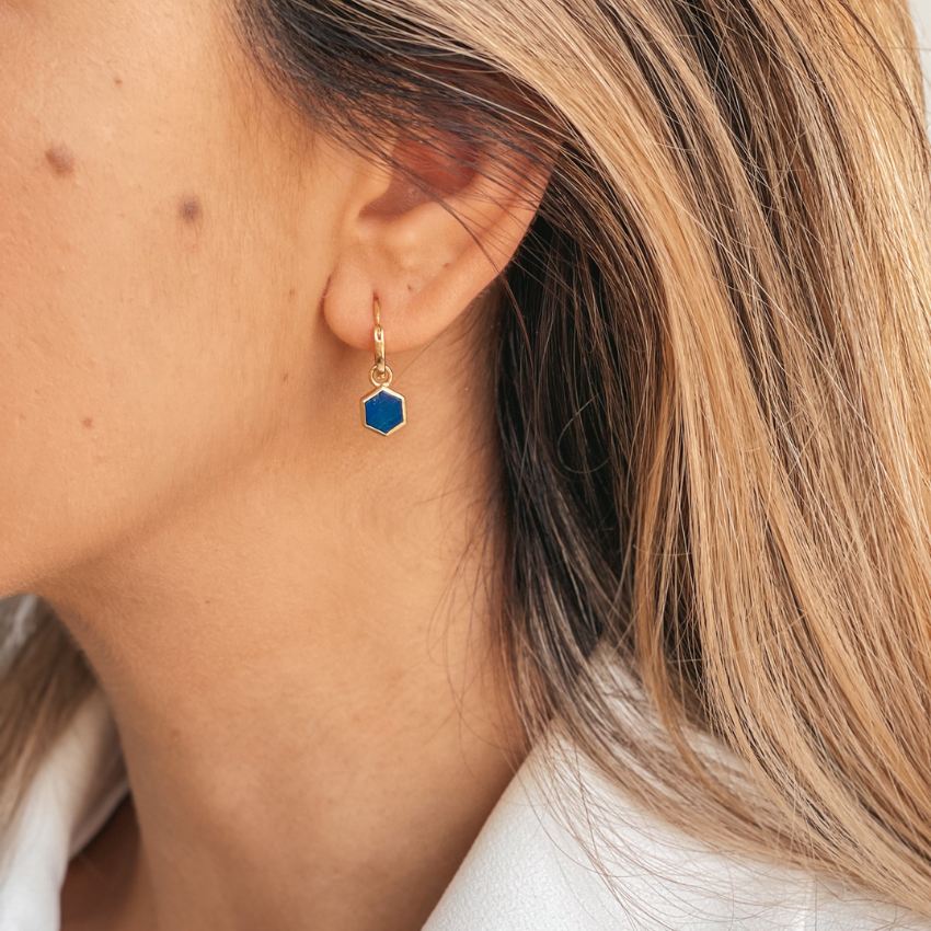 Primo piano di un orecchio femminile che indossa un orecchino dorato con una pietra esagonale blu, identificata come Lapislazzuli.