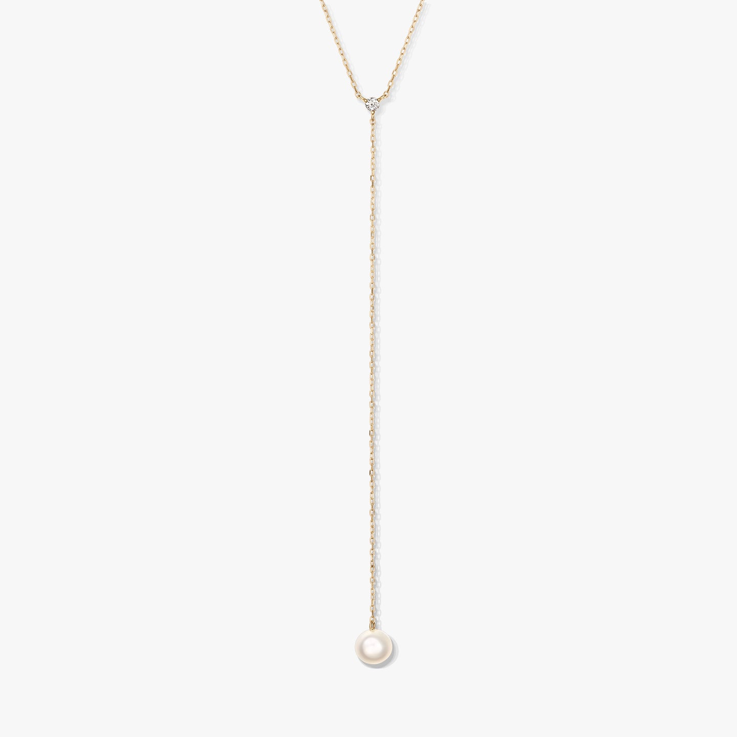 Collana lariat minimalista in oro con una singola perla bianca rotonda pendente e una piccola pietra d'accento, al centro su sfondo bianco.
