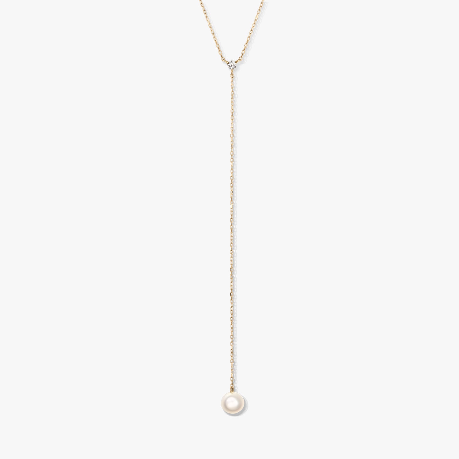 Collana lariat minimalista in oro con una singola perla bianca rotonda pendente e una piccola pietra d'accento, al centro su sfondo bianco.