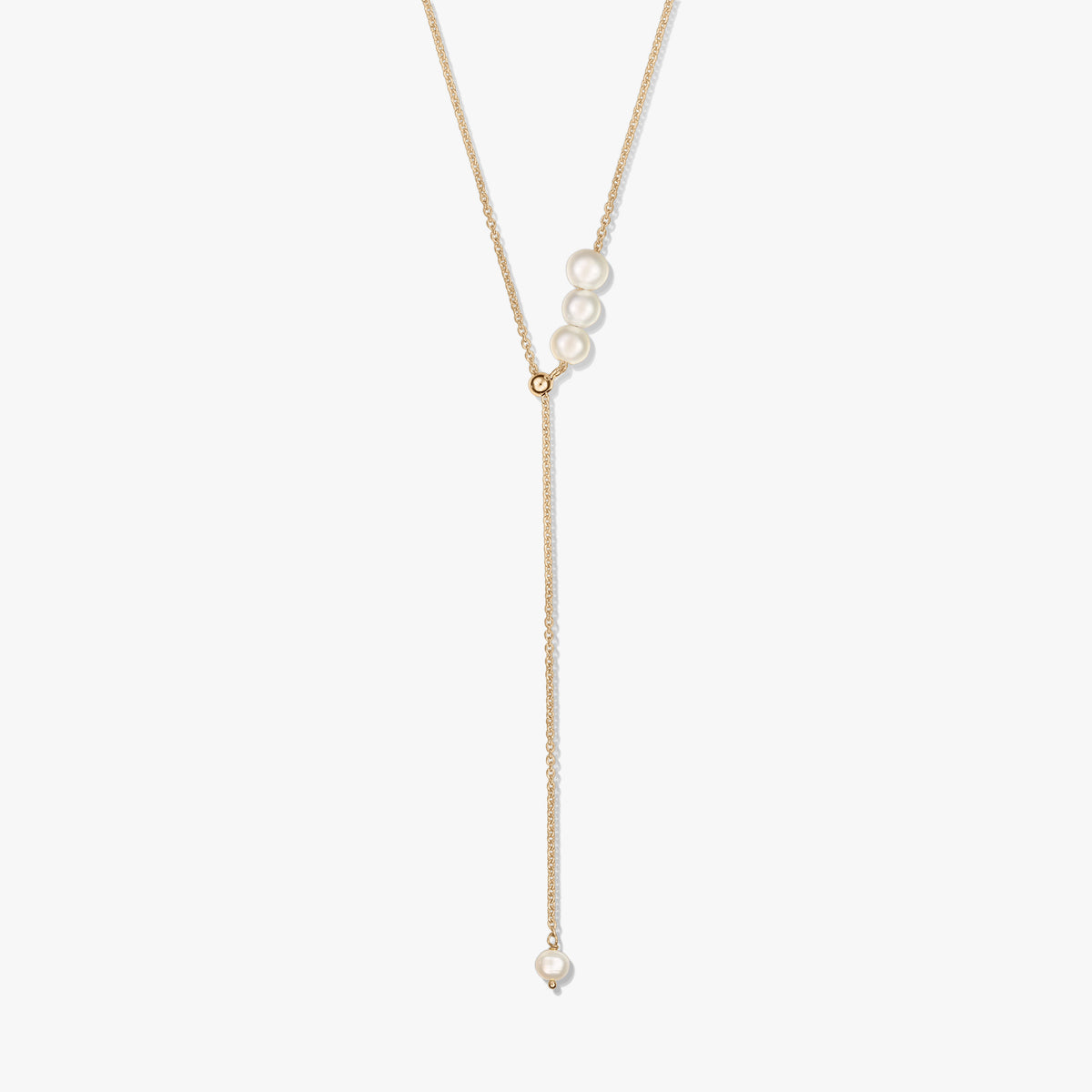 Delicata collana lariat in argento sterling placcato oro con un trio di perle coltivate al cursore scorrevole e una singola goccia di perla, su sfondo bianco.