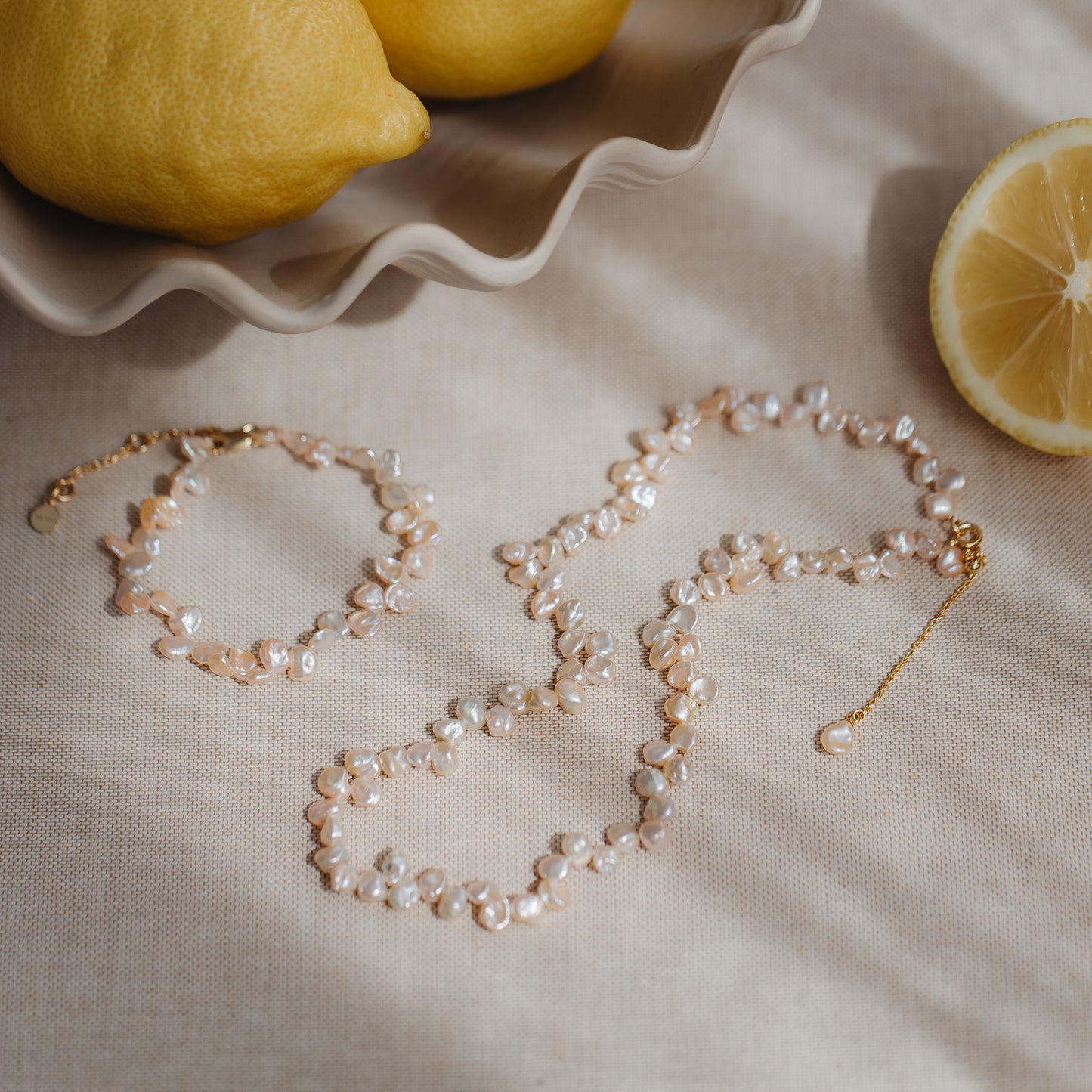 Elegante collana in argento placcato oro con perle keshi rosa, su lino neutro con limoni; accanto, un bracciale coordinato.