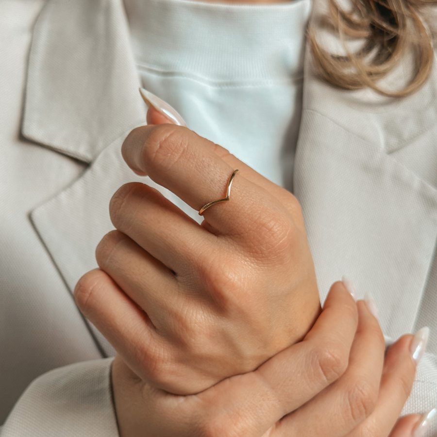 Una persona con un semplice anello d'oro a forma di V sul dito, vestita con un abito chiaro.