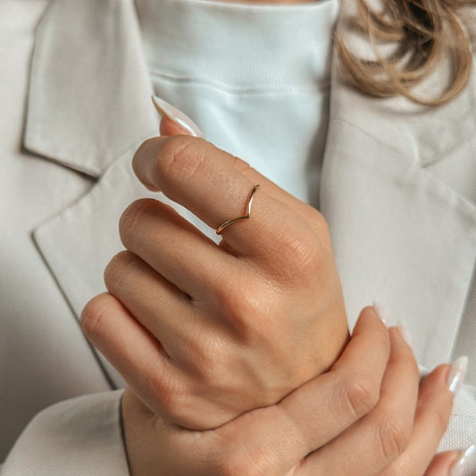 Una persona con un semplice anello d'oro a forma di V sul dito, vestita con un abito chiaro.