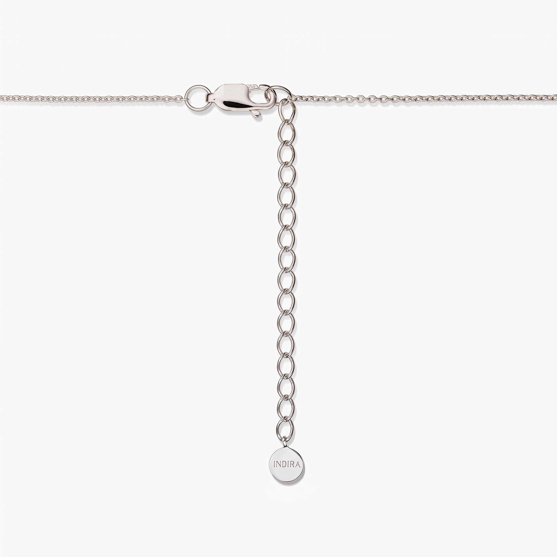 Primo piano della chiusura di una collana in argento sterling con catenina di prolunga regolabile e una piccola targhetta rotonda incisa “INDIRA”, su sfondo bianco.