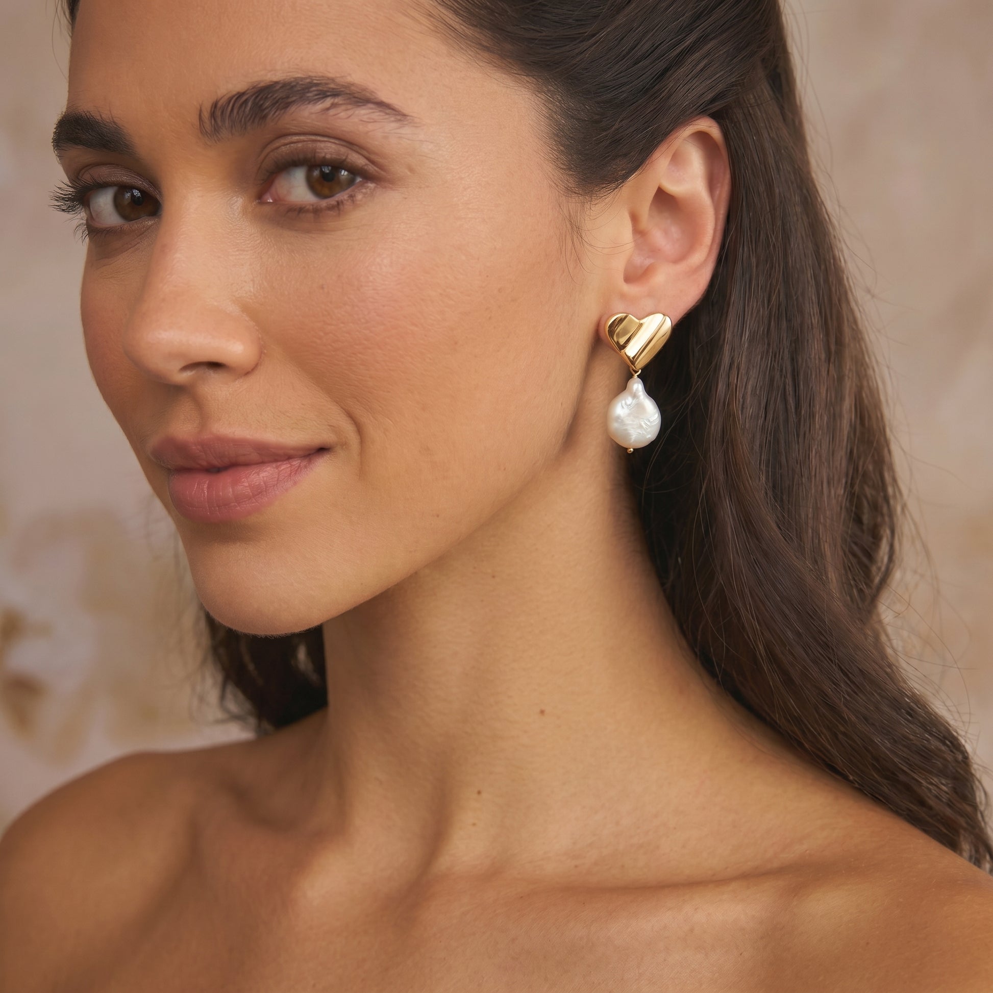 Primo piano di una donna che indossa un orecchino in argento placcato oro a forma di cuore con una pietra naturale pendente a forma di pera.