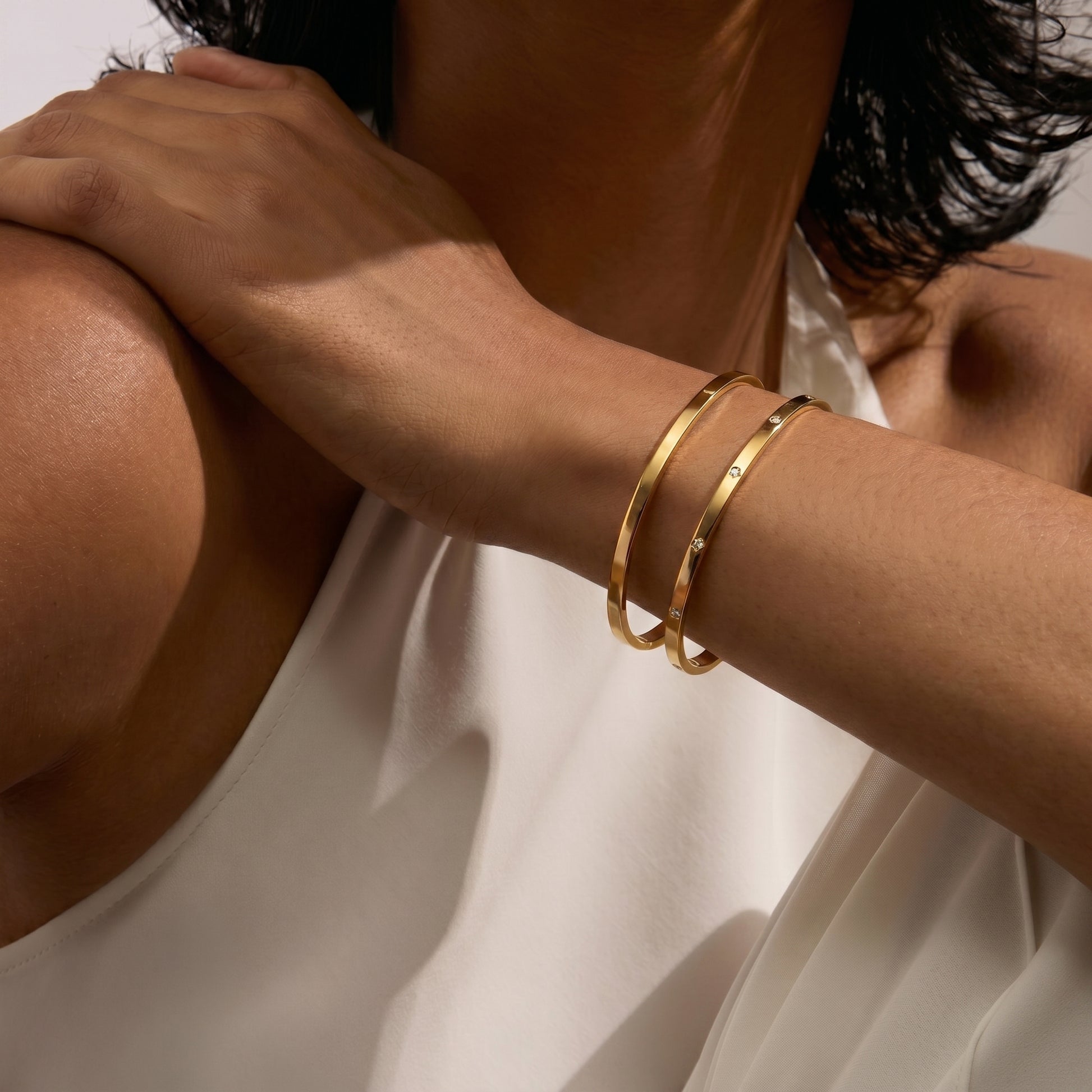 Primo piano di un braccio con indosso due bracciali a cerchio in oro su sfondo bianco.