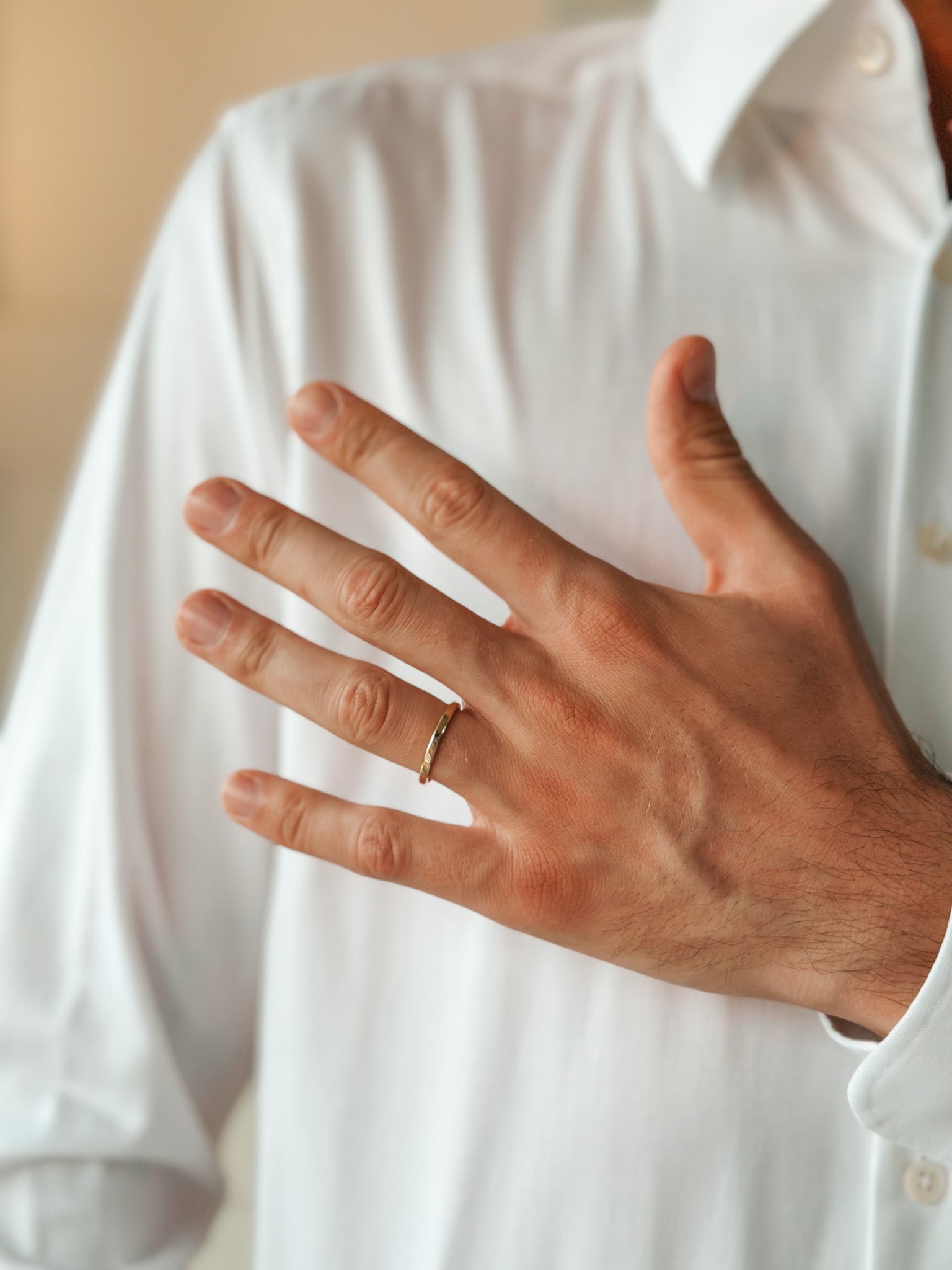 A hand wearing a gold wedding ring on the ring finger, resting against a white shirt.