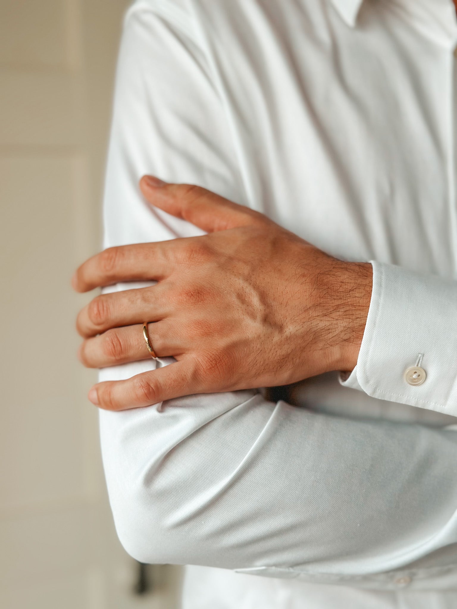 Close-up of a person wearing a white shirt and a thin gold wedding band on their finger.