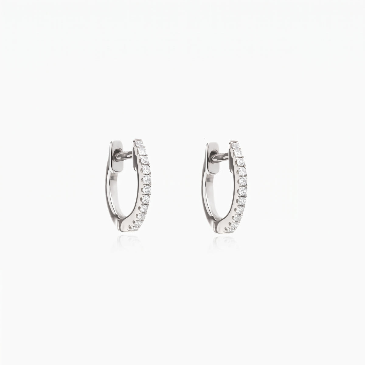 Coppia di orecchini a cerchio huggie Sadie in argento con zirconi trasparenti a pavé, su sfondo bianco.