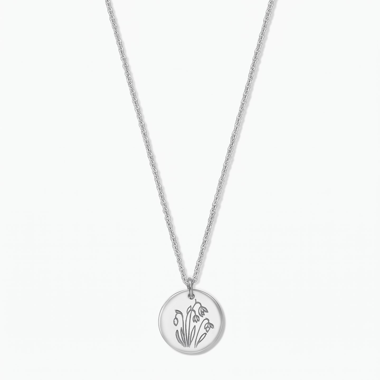 Collana in argento sterling con fiore di nascita, ciondolo a disco rotondo inciso con i bucaneve di gennaio su una catena fine, isolata su sfondo bianco.