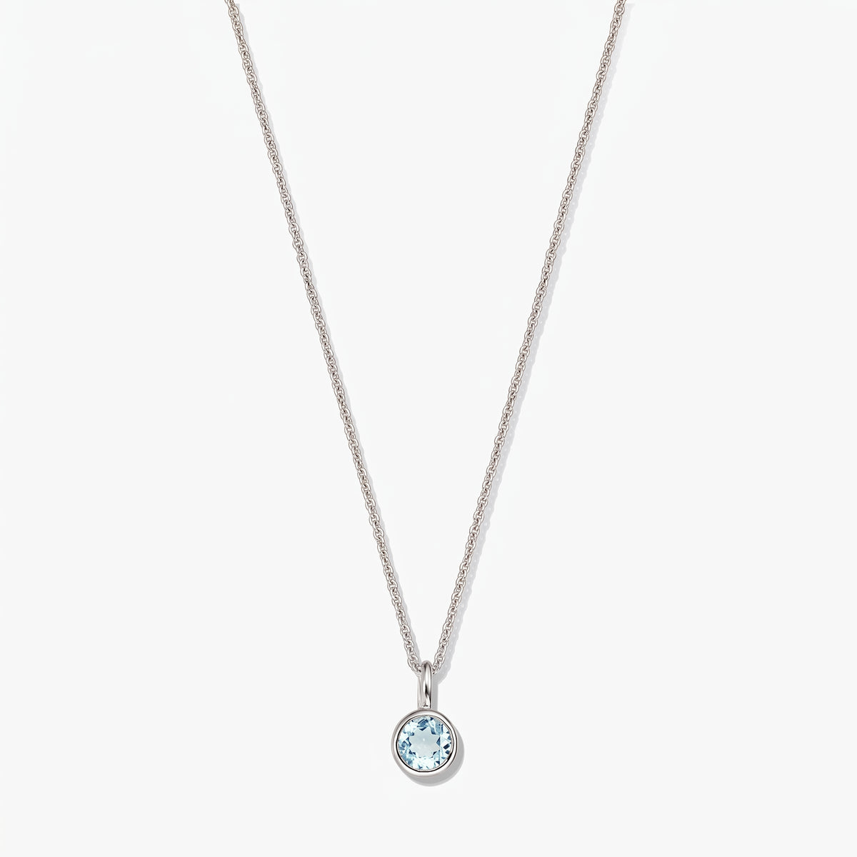 Elegante collana in argento sterling con pietra di nascita e piccolo ciondolo rotondo in topazio blu con montatura a castone, su sfondo bianco.