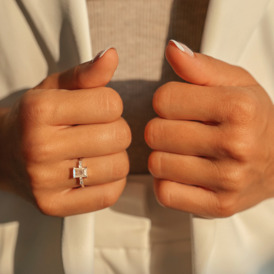 Immagine ravvicinata di mani che indossano un Evie Silver Ring con una pietra di luna, con un abbigliamento bianco, che mostrano i pollici intrecciati.