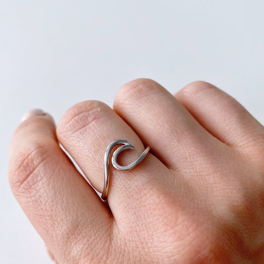 Primo piano di una mano che indossa un anello minimalista in argento con design a onda.