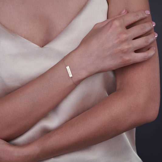 Primo piano di una persona che indossa un braccialetto in oro 14K con la scritta 'Loved' incisa, su uno sfondo neutro.