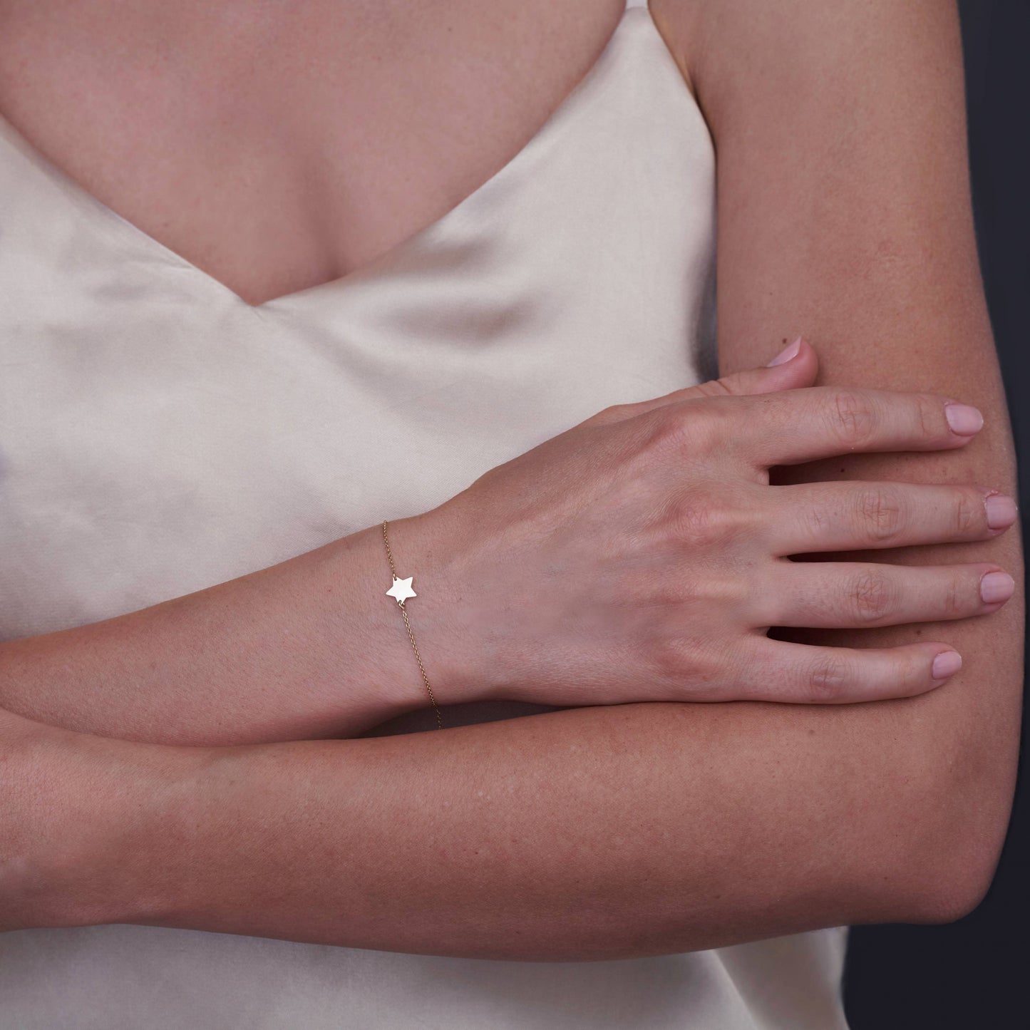 Un braccio femminile indossa un delicato bracciale a stelle in oro 14K su una blusa di satin chiara.