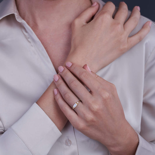 Primo piano delle mani di una donna che indossa un anello d'oro con pietra di luna e zirconia, su uno sfondo neutro.