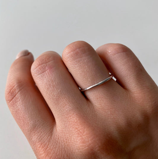 Una mano che indossa un semplice anello d'argento su uno sfondo chiaro.