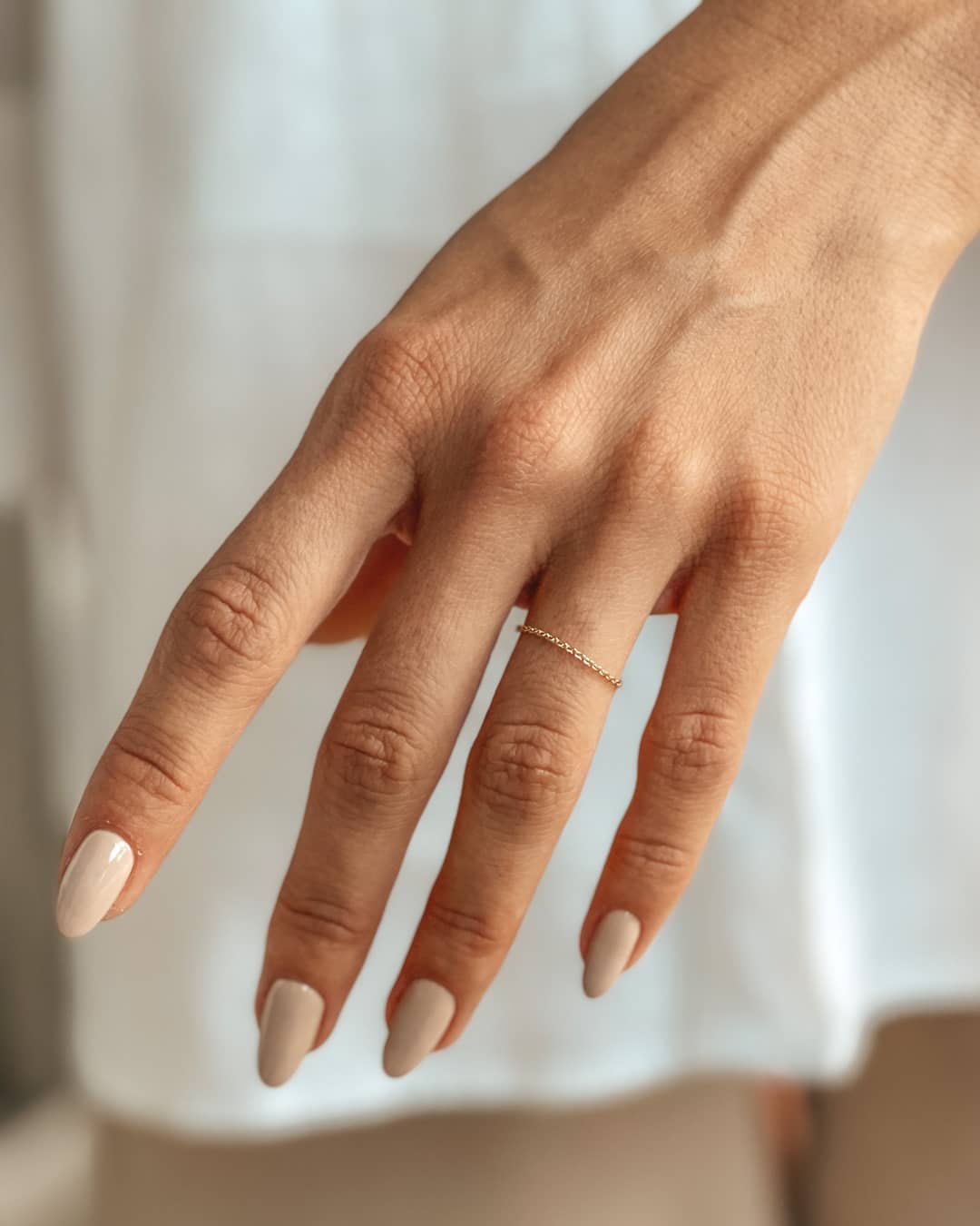 Una mano delicata con un anello a catena in oro 14K e unghie manicure nude.