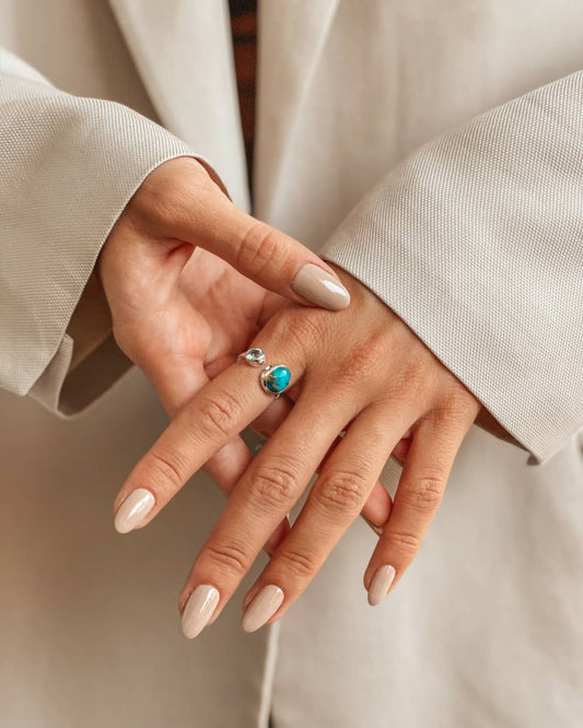Primo piano di mani che mostrano un anello in argento con pietre di topazio blu e turchese.