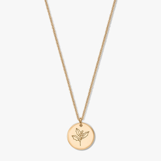 Collana in argento sterling placcato oro con ciondolo a disco rotondo inciso con motivo di agrifoglio (fiore del mese di dicembre) su sfondo bianco.