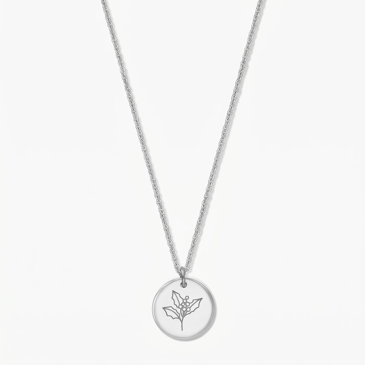 Collana in argento sterling con fiore di nascita, ciondolo rotondo inciso con un rametto di agrifoglio, su sfondo bianco.