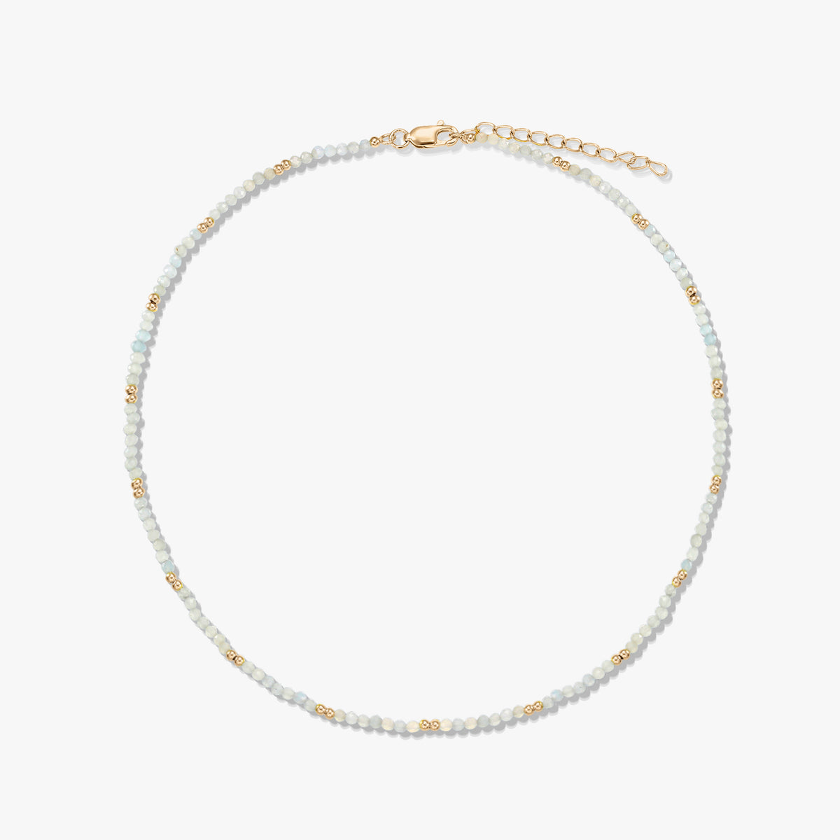 Collana delicata a perline di pietra di luna con piccole perline distanziatrici dorate e chiusura a moschettone con prolunga in argento sterling placcato oro, disposta in cerchio su sfondo bianco.