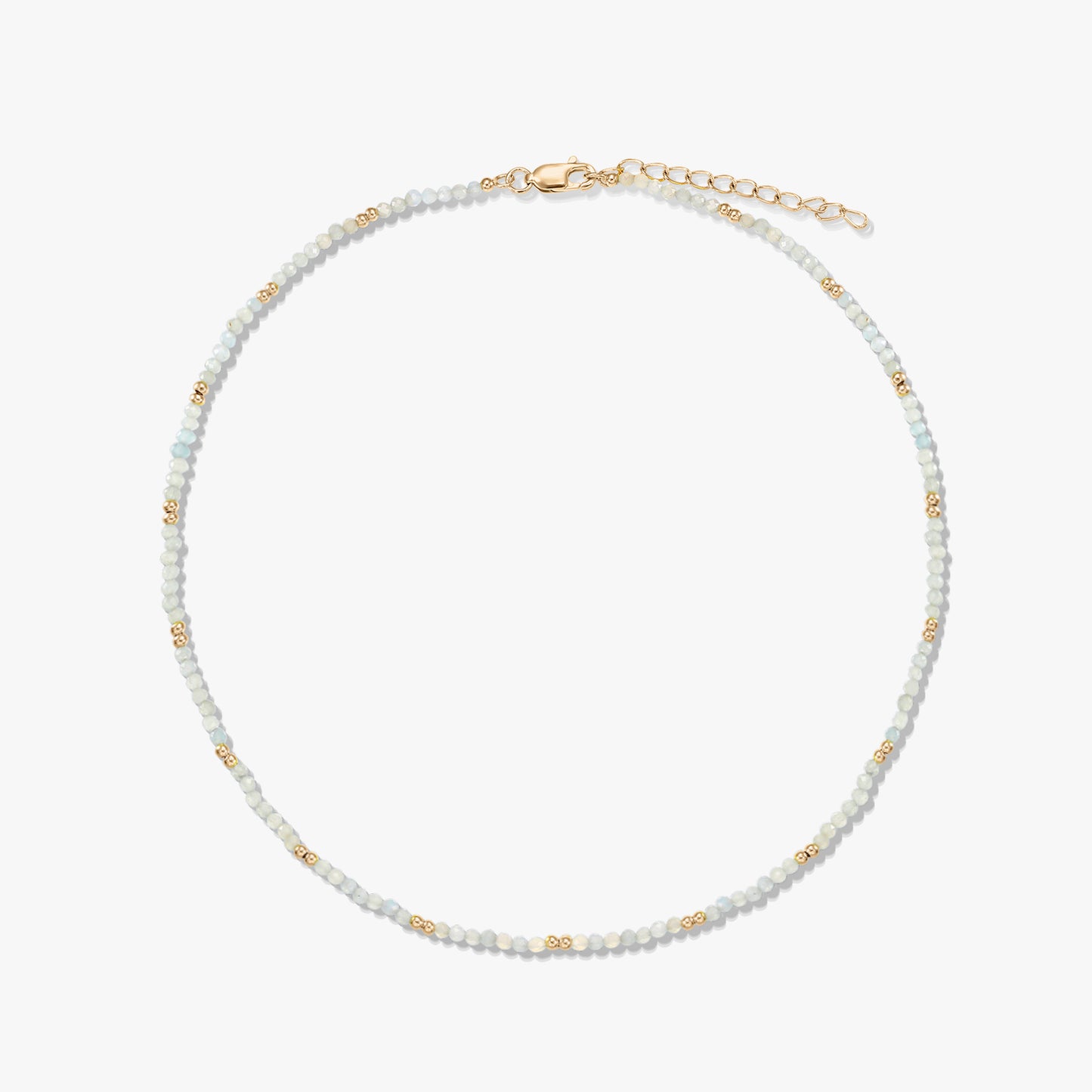 Collana delicata a perline di pietra di luna con piccole perline distanziatrici dorate e chiusura a moschettone con prolunga in argento sterling placcato oro, disposta in cerchio su sfondo bianco.