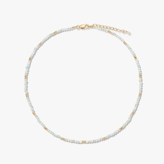 Collana delicata a perline di pietra di luna con piccole perline distanziatrici dorate e chiusura a moschettone con prolunga in argento sterling placcato oro, disposta in cerchio su sfondo bianco.