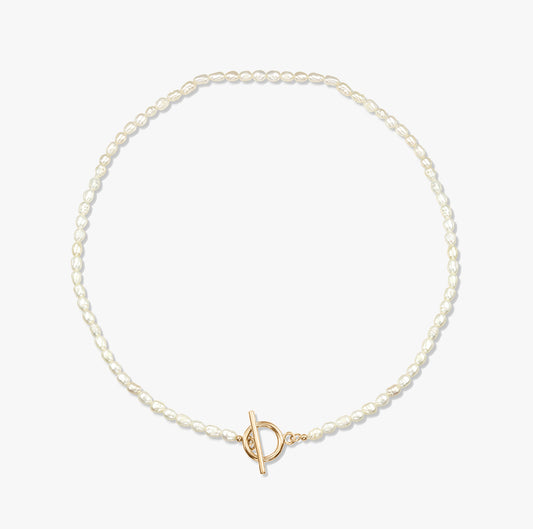 Collana minimalista con perla e chiusura a T in oro su sfondo bianco.