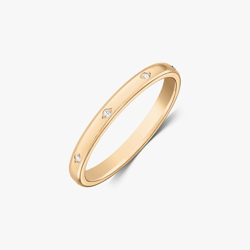Scatto in studio angolato di una fede nuziale sottile in oro giallo 14K con piccoli diamanti incastonati a filo, su sfondo bianco.
