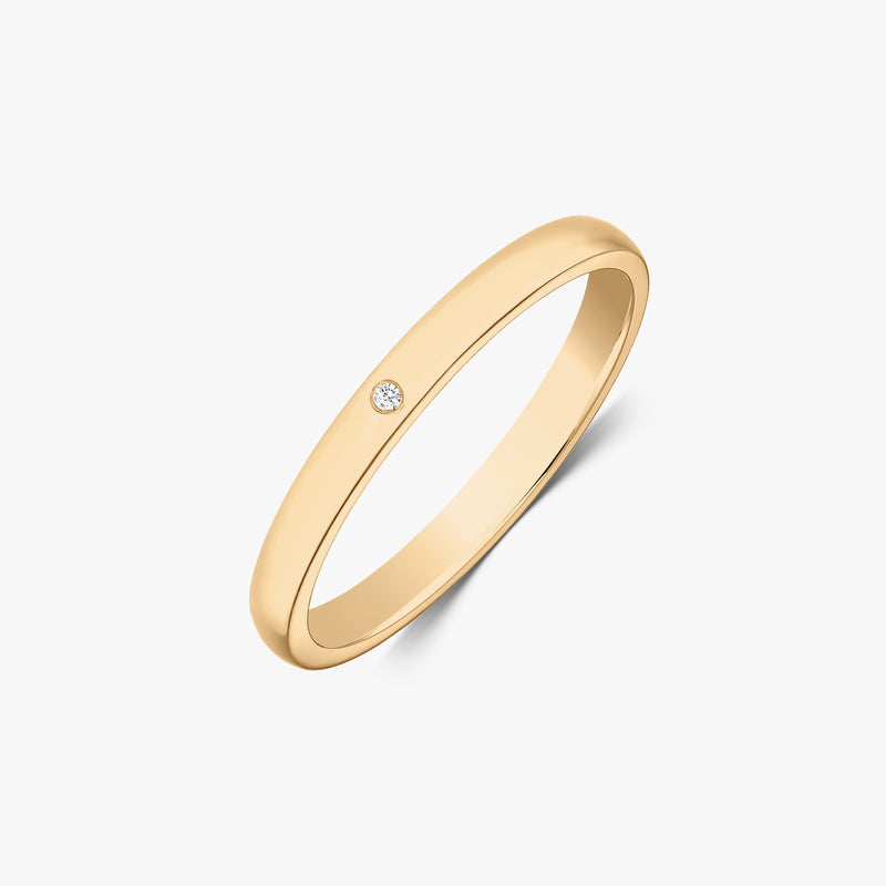 Fede nuziale sottile in oro giallo 14k con un piccolo diamante rotondo incassato a filo, vista angolata su sfondo bianco.