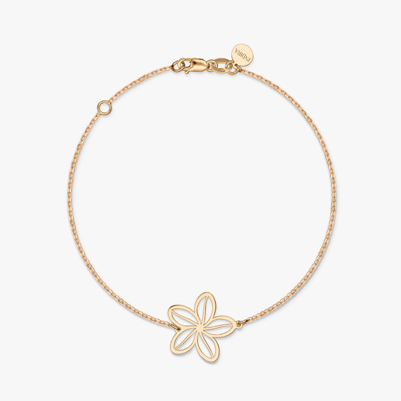 Un braccialetto minimalista in oro con un delicato ciondolo a forma di fiore su uno sfondo bianco solido.