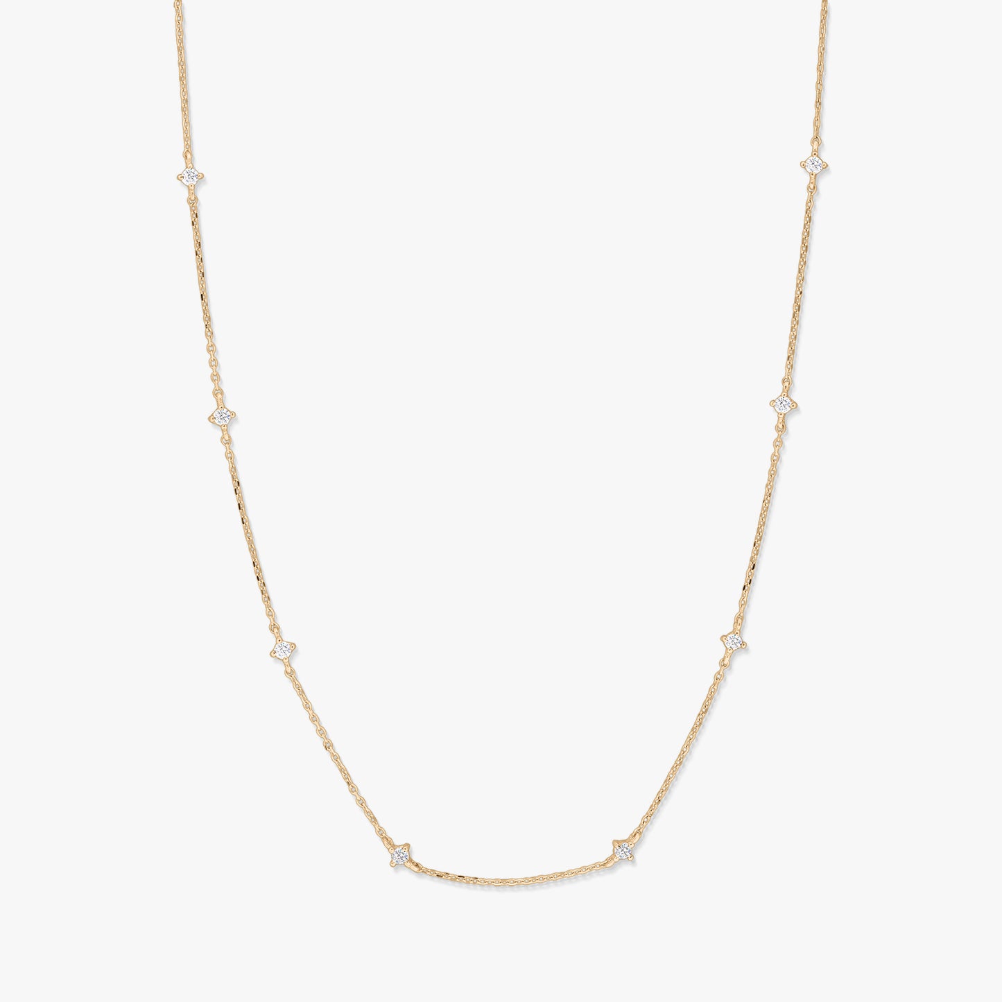Collana station in oro giallo 14K con piccoli accenti di zirconi bianchi a forma di stella raggiante, distanziati lungo una catena sottile, fotografata su sfondo bianco.