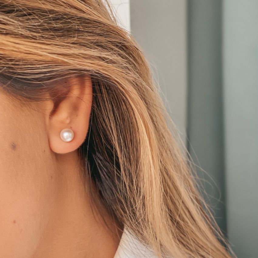 Primo piano di un orecchio femminile con un classico orecchino a bottone di perle.