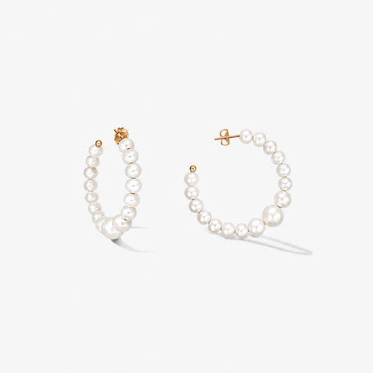 Coppia di orecchini a cerchio in argento sterling placcato oro con perle naturali bianche a scalare su sfondo bianco.