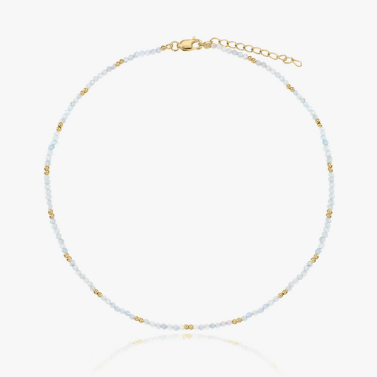 Collana delicata con perline di pietra di luna, piccoli dettagli dorati e chiusura regolabile placcata in oro, su sfondo bianco.