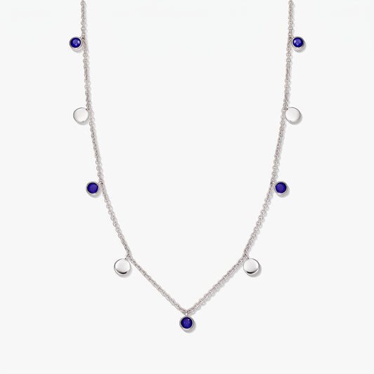 Collana a stazioni in argento sterling con cabochon rotondi di lapislazzuli e dischi in argento lucido su sfondo bianco.