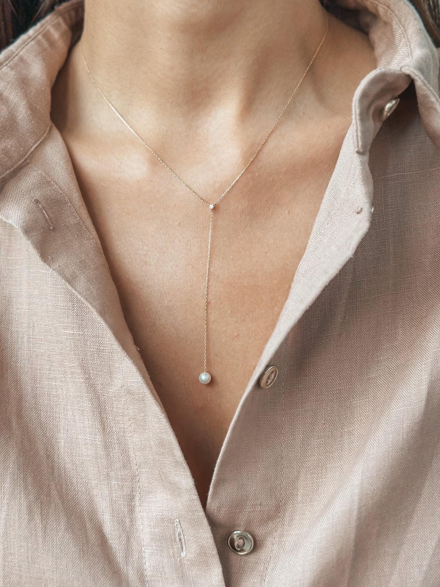 Primo piano di una delicata collana d'oro con ciondolo di perla indossata su una camicia con colletto aperto.
