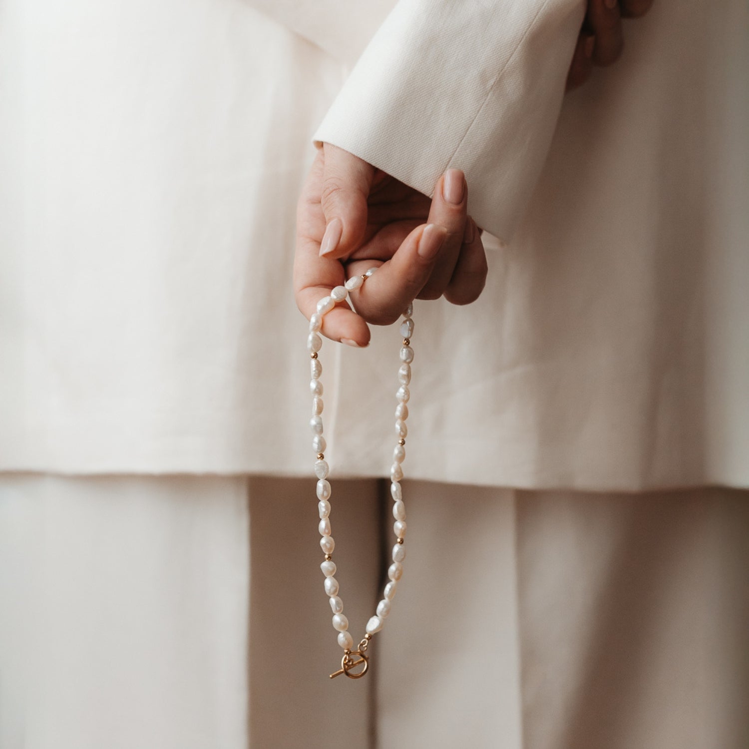Primo piano di una mano che tiene una collana d'argento con perle naturali.