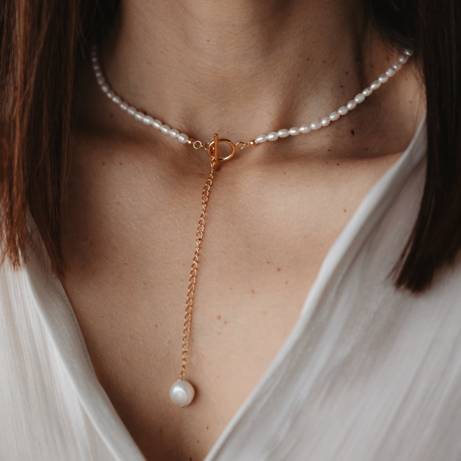 Primo piano del collo di una donna con una collana in argento e ciondolo con perla naturale, e catena in oro.