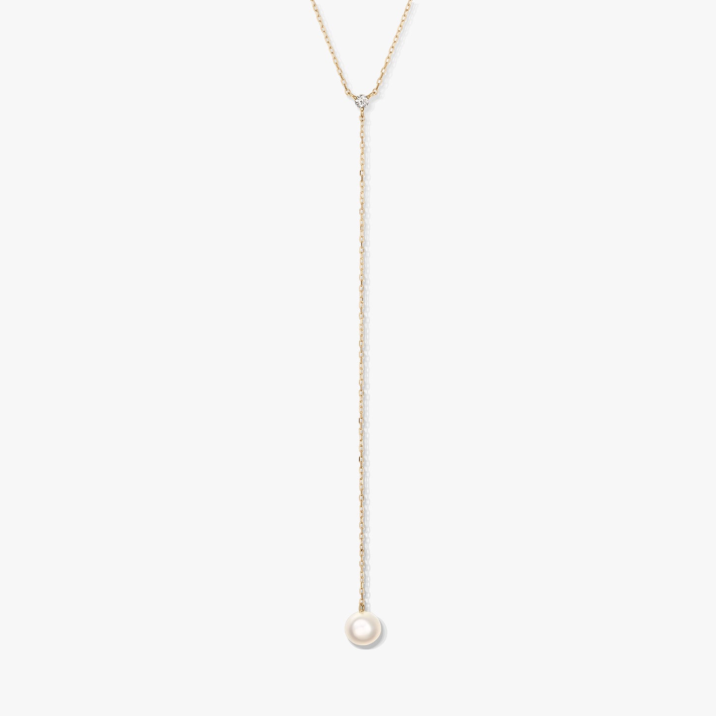 Collana lariat minimalista in oro con una singola perla bianca rotonda pendente e una piccola pietra d'accento, al centro su sfondo bianco.