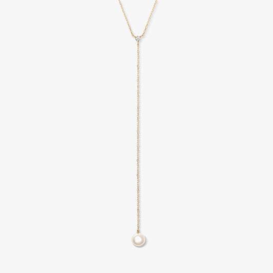 Collana lariat minimalista in oro con una singola perla bianca rotonda pendente e una piccola pietra d'accento, al centro su sfondo bianco.