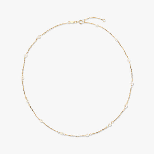 Elegante collana a stazioni in oro giallo 14K con piccole perle bianche naturali distanziate lungo una catenina sottile, isolata su sfondo bianco.