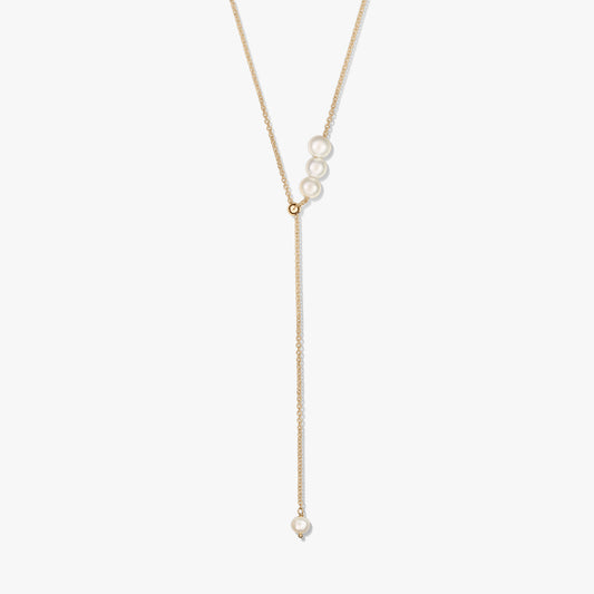 Delicata collana lariat in argento sterling placcato oro con un trio di perle coltivate al cursore scorrevole e una singola goccia di perla, su sfondo bianco.