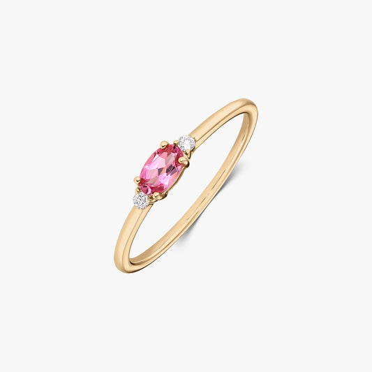 Anello in oro giallo 14K con tormalina rosa ovale centrale affiancata da due piccoli diamanti rotondi su una fascia sottile, su sfondo bianco.