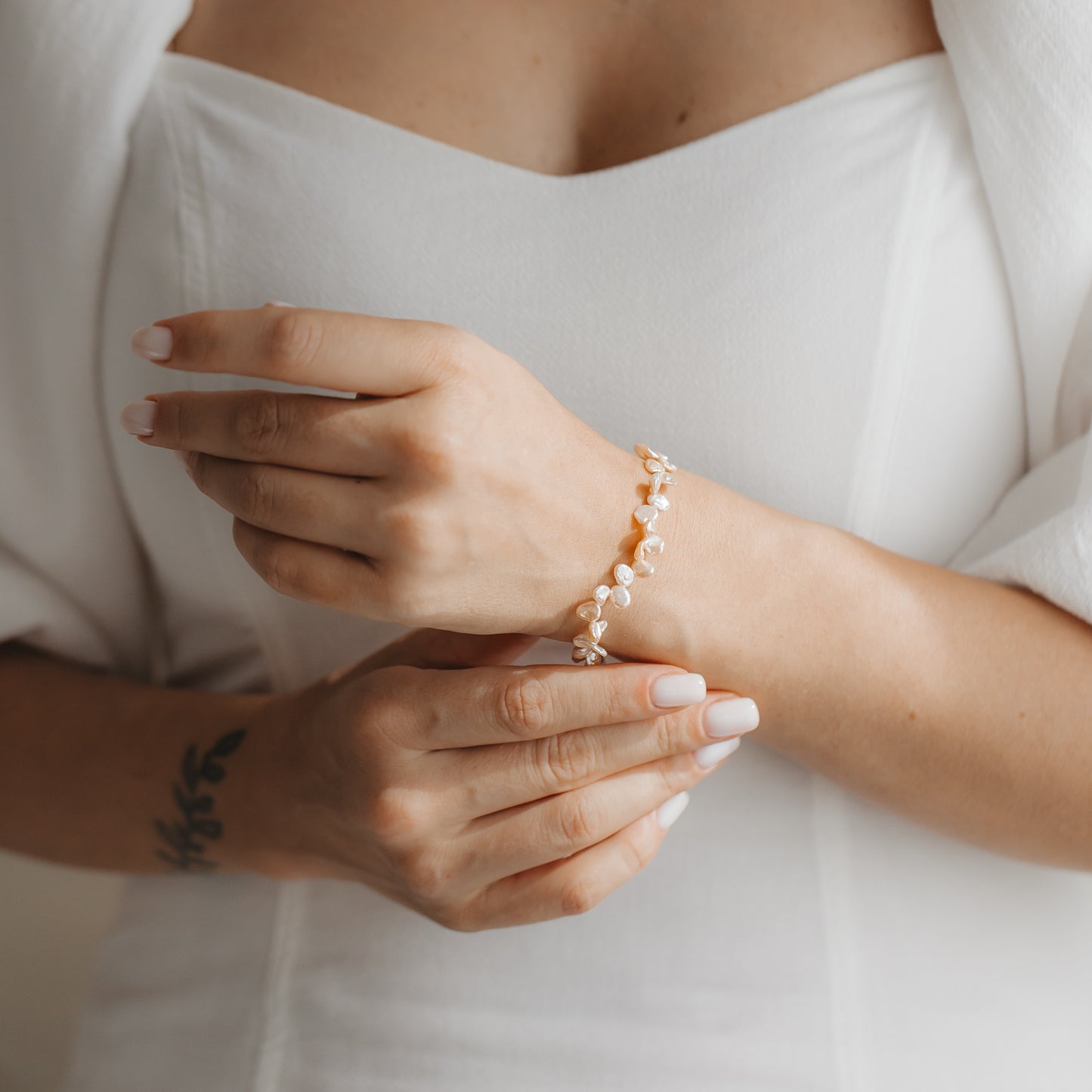 Primo piano delle mani che indossano un delicato bracciale in argento sterling con perle keshi rosa, abbinato a un abito bianco.
