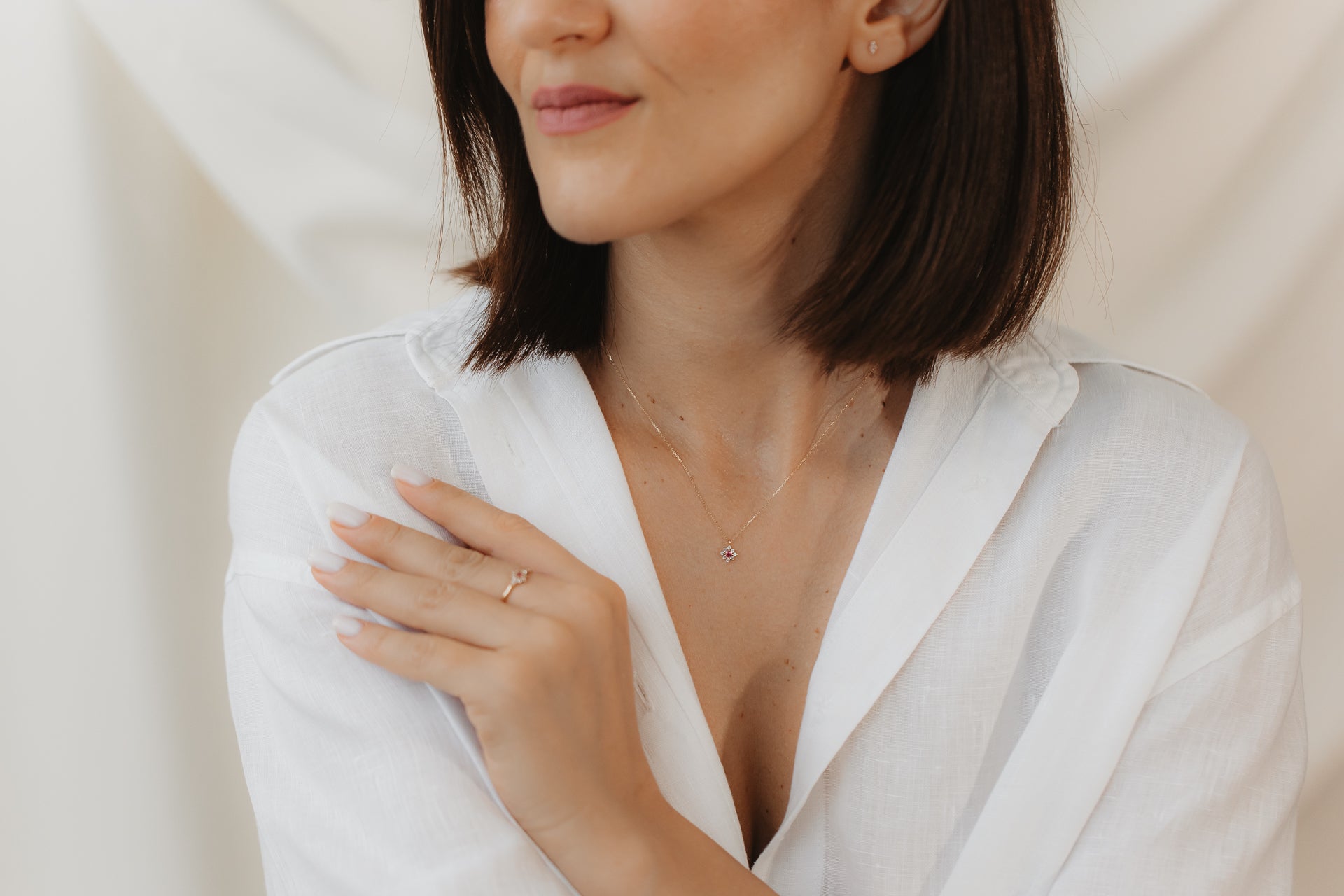 Primo piano di una persona con camicetta bianca che indossa un delicato anello in oro giallo 14K con tormalina rosa e zaffiro bianco, mano appoggiata sulla spalla su uno sfondo morbido e neutro.